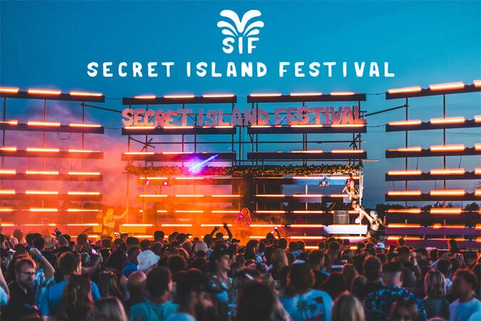 Secret Island Festival, very cool photo showing 2 women with fluffy hats and cuffs, sequin outfits, and eye-glasses with neon lights around the frames and across the eyes.