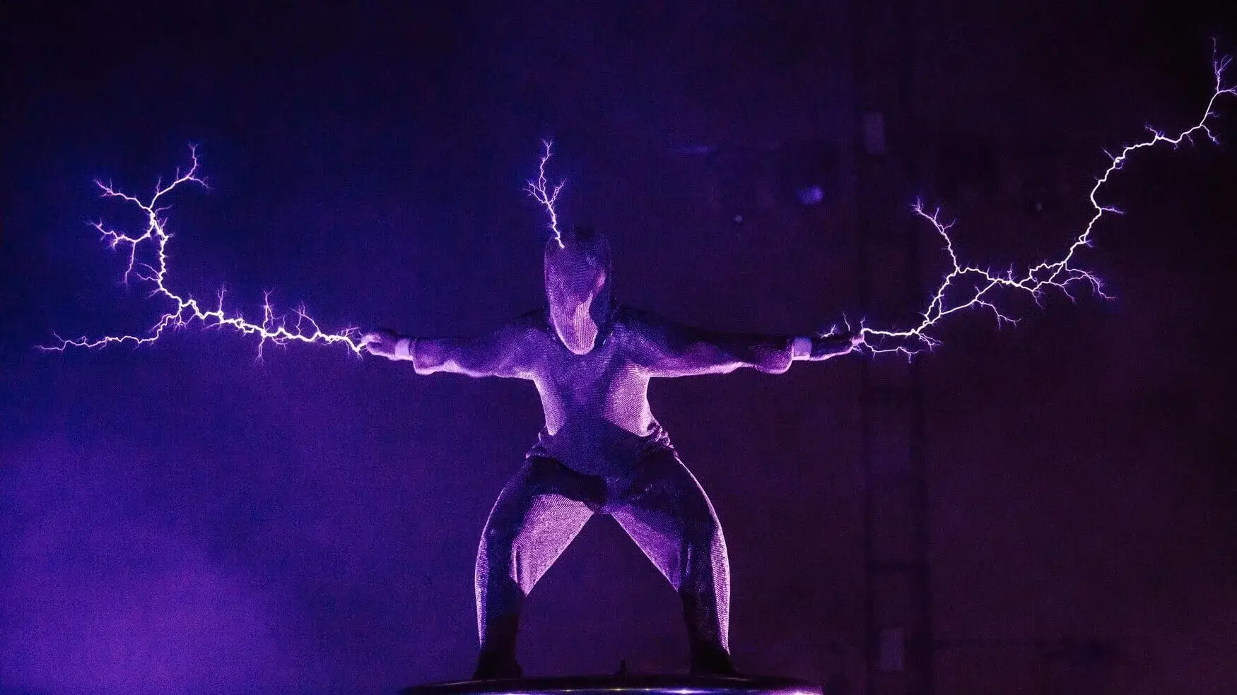 Wilderness festival performance photo showing person in chain-mail suit with electricity sparks coming out from head and hands.