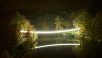 Beam of warm white light across a river illuminating reflection at the Lumiere Festival, Durham