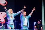 Two singers raising their arms while performing together on stage. Photograph by Will Bailey Photography.