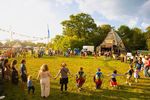 Festival goers hand in hand making a large circle on a green field in the sunshine, with children and adults.